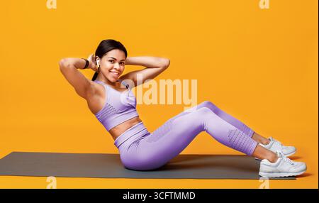Millennial african american woman doing abs exercises on sports mat over yellow studio background Stock Photo