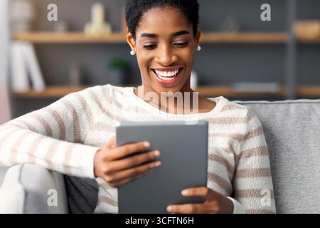 Smiling African American Woman Relaxing On Sofa With Digital Tablet At Home Stock Photo