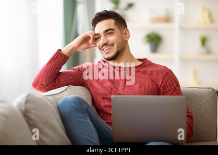 Dreamy arab guy sitting on sofa with laptop Stock Photo