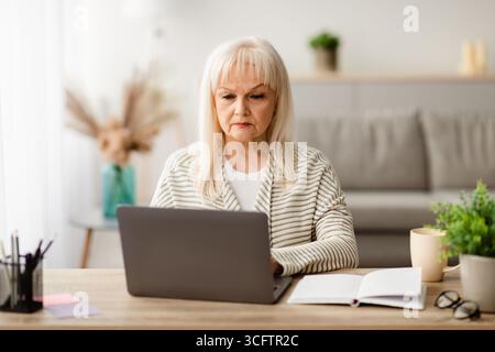 Focused mature woman sitting ot desk and working on computer Stock Photo