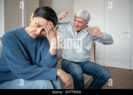 Elderly man waving arms in agitation toward weary wife bears constant arguments accusations, tension Stock Photo