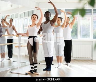 Group mastering third position at barre in ballet studio Stock Photo