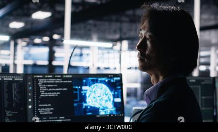 Data center software developer using computer to monitor neural network AI LLM visualization. Worker in high tech facility using PC to oversee servers powering machine learning processes, camera A Stock Photo
