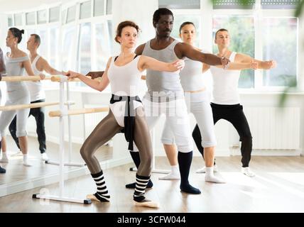 Female ballet instructor practicing demi plie at barre with students Stock Photo