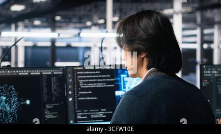 Technician arriving in data center office, coding with generative AI assistance. IT expert sitting at desk, starting work on artificial intelligence large language model solving tasks, camera A Stock Photo