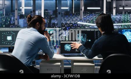 Server room system administrators using AI to review infrastructure diagnostics. IT professionals in data center analyzing performance data using artificial intelligence technology, camera A Stock Photo