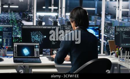 Programmer entering server room office, using AI to review infrastructure diagnostics. IT admin in data center high tech facility analyzes performance data using artificial intelligence tech, camera A Stock Photo