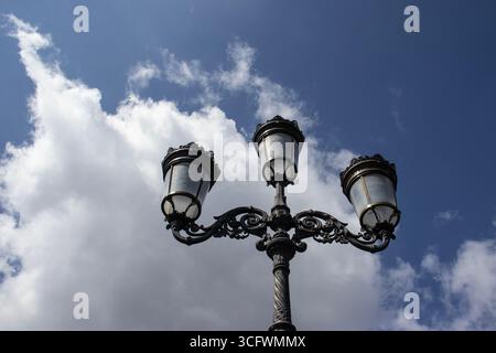 Three ornate street lamps on a post against clouds in a blue daytime sky. Photographed on O'Connell Bridge across the Liffey River in Dublin, Ireland. Stock Photo