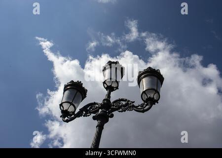 Three ornate street lamps on a post against clouds in a blue daytime sky. Photographed on O'Connell Bridge across the Liffey River in Dublin, Ireland. Stock Photo