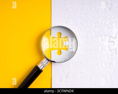 Magnifying glass focusing on a missing puzzle piece, representing recruitment, hiring the right candidate, solving problems, solutions, job search, va Stock Photo
