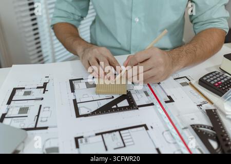 Architect working at desk with architectural blueprints, holding a pencil for sketching or adjustments. Professional workspace with tools and equipmen Stock Photo