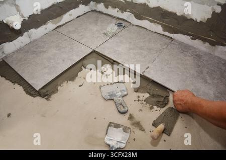 Builder installing ceramic tile on the floor, bathroom flooring. Floor tiling Stock Photo
