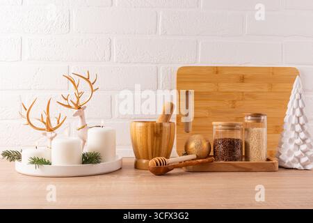 Beautiful kitchen background of Christmas kitchen countertop with spice jars, mortar and pestle, dish with candles and reindeer. Front view Stock Photo