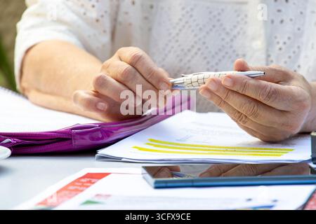 A woman is holding a pen over a piece of paper. There is something written on the paper. The important part is highlighted in yellow. Stock Photo