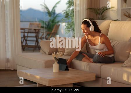 Yogi preparing online yoga class on tablet sitting on a sofa at sunset in a house Stock Photo