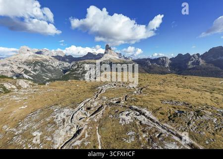 Aerial view of rugged Monte Piana trenches snaking through golden grasslands under a vast blue sky meeting distant, jagged Dolomite peaks, Misurina, Trentino-South Tyrol, Italy. Stock Photo