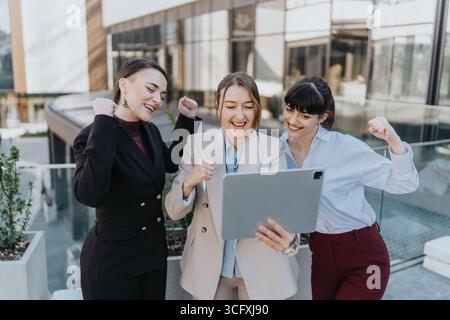 Three female professionals celebrating success while collaborating on a digital project outdoors Stock Photo