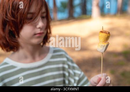 Cute girl eats marshmallows roasted over a campfire on a camping trip Stock Photo