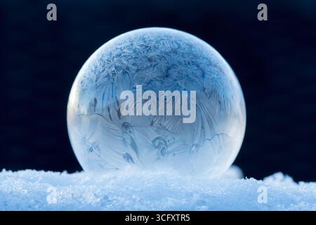 Frozen soap bubble on snow, winter magic of frozen soap bubble with beautiful ice crystals in perfect sphere on snow with blurred background Stock Photo