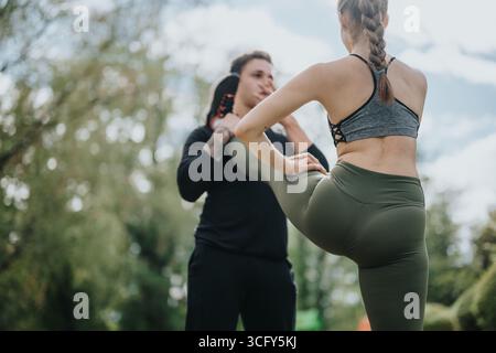 Fitness trainer assists woman in stretching outdoors Stock Photo