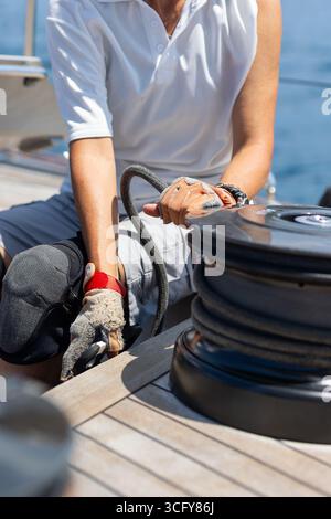 A close-up of a man with sailing gloves working on the sheet. The photo captures the action of sailing, highlighting the passion for sailing Stock Photo