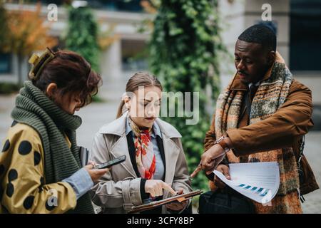 Multiracial Colleagues Collaborating Outdoors with Documents and Devices Stock Photo