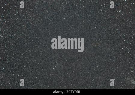 Dark asphalt pavement with fine grain with light patches, close-up. Stock Photo