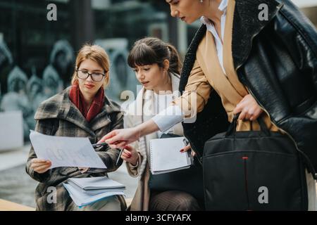 Three businesswomen collaborating outdoors while analyzing documents and notes together. Stock Photo
