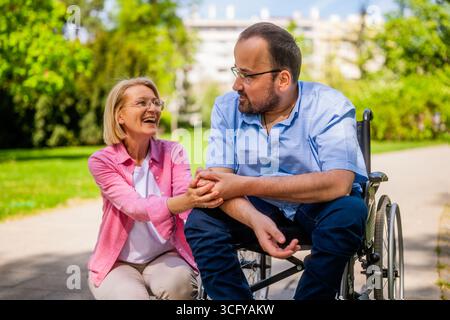 Man in wheelchair is spending time with his friend in park. Stock Photo