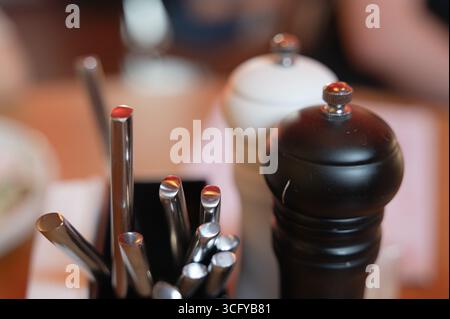Close-up of a condiment holder featuring various utensils and pepper grinder in a cozy restaurant environment, highlighting dining essentials. Stock Photo