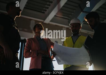 Construction team reviewing blueprints at an active site with collaboration and problem-solving Stock Photo