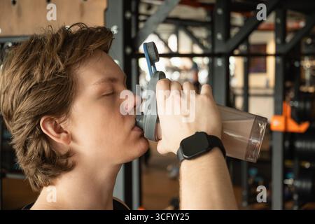 Bodybuilder or sporty young caucasian man drinking protein shake at gym. Working out. Stock Photo