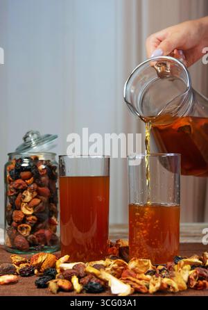 Hand pouring dried fruit compote into glasses with scattered fruits Stock Photo