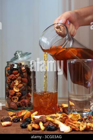 Hand pouring dried fruit compote into glass with jar and scattered fruits Stock Photo