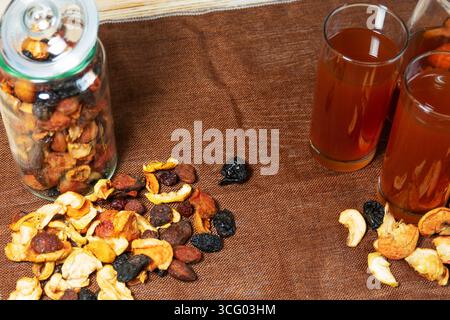 Glasses of dried fruit compote with jar and scattered fruits on brown cloth Stock Photo
