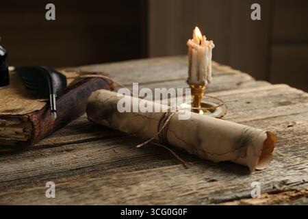 Old paper scroll, book, feather and burning candle on wooden table, closeup Stock Photo