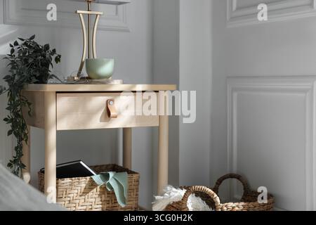 Bedside table with lamp and other decor near bed indoors Stock Photo