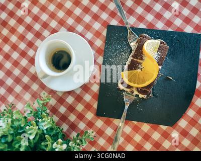 Tempting chocolate cake adorned with vibrant orange slices, paired with a rich espresso, set on a classic checkered tablecloth with greenery Stock Photo