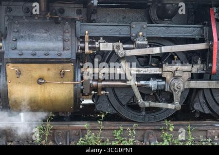 Close-up view of vintage steam locomotive drive wheels and connecting rods showing yellow cylinder housing, black mechanical components Stock Photo
