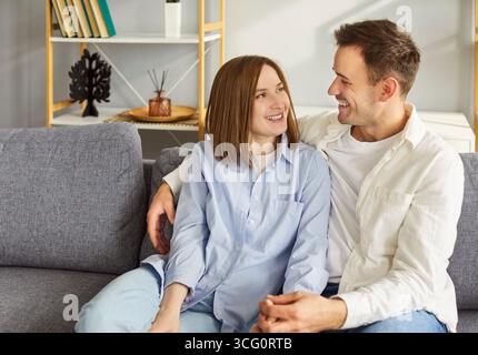 Portrait of married couple in love at home, posing smiling seated on couch in modern living room Stock Photo