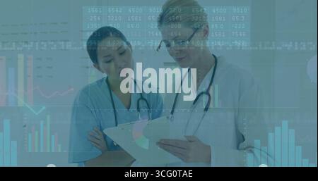 Reviewing charts, two doctors analyzing data overlays in exam room, with clipboard and stethoscopes Stock Photo