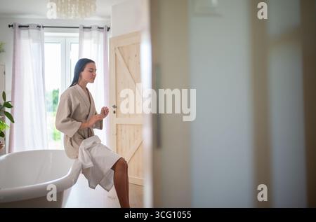 young woman enjoying hair care routine in cozy bathroom. Stock Photo
