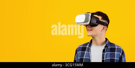 Cool guy in VR headset exploring cyberspace, using virtual reality for entertainment or studies on orange background Stock Photo