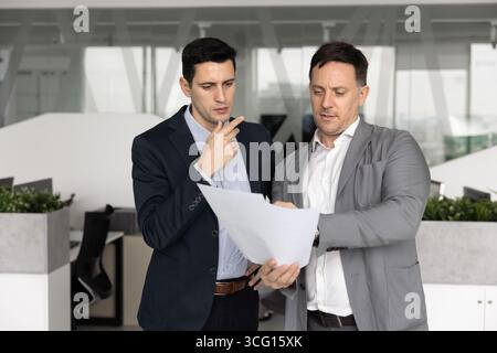 Two mature and young male colleagues discussing presentation or report Stock Photo