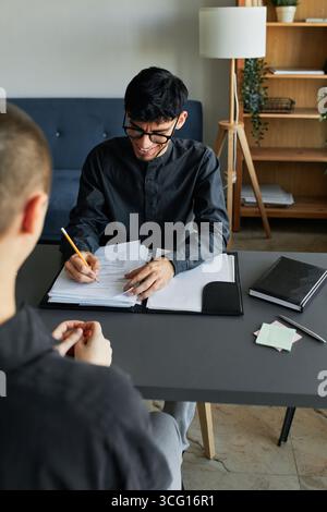 Vertical high angle shot of unrecognizable stylish young woman with short hair sitting in front of joyful HR manager talking about her work experience Stock Photo