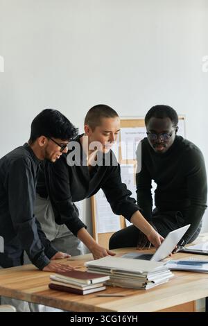 Group of three ethnically diverse young people wearing casual outfits working together on new project in modern office Stock Photo