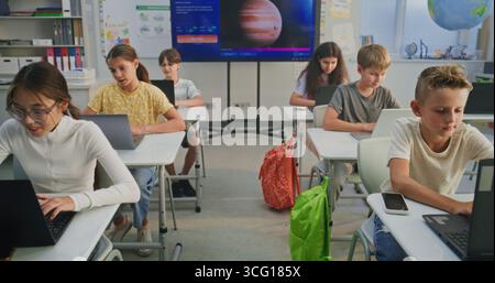Elementary School Children Using Laptops, Doing Creative Tasks During Digital Art Lesson in Classroom. Digital Screen Showing AI Software for Creating Pictures. Interactive STEM Education. Dolly Shot. Stock Photo