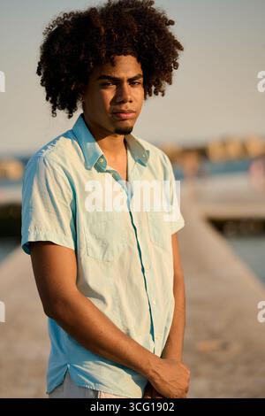 Young man with afro hair posing on pier at sunset Stock Photo