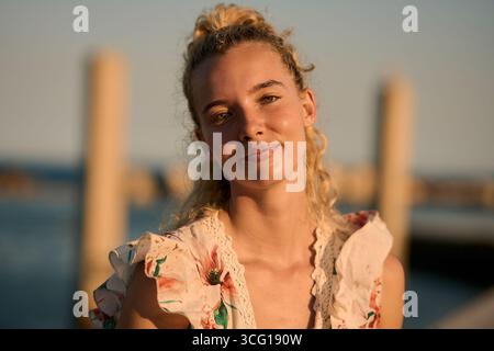Blonde woman smiling at golden hour by the sea Stock Photo