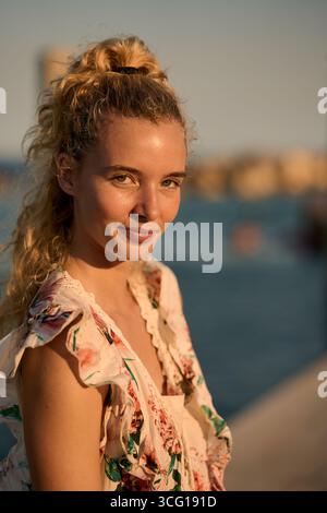 Blonde woman smiling by the sea at golden hour Stock Photo
